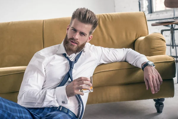 Hombre de negocios deprimido sosteniendo vaso de whisky en la sala de estar. vestido con camisa blanca . — Foto de Stock