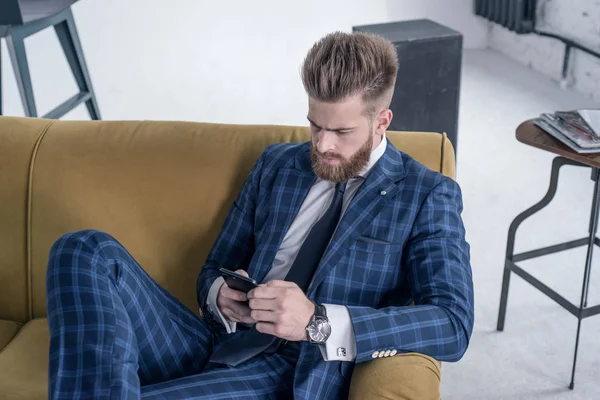 Vista superior de la hermosa sexy hombre de negocios sentado en un sofá en un traje y utilizando su teléfono —  Fotos de Stock