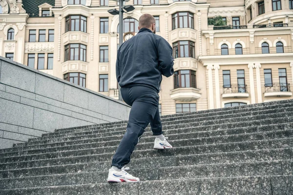 Sport hard. Close up of male feet climbing stairs outside. Well shaped man is jogging at dawn