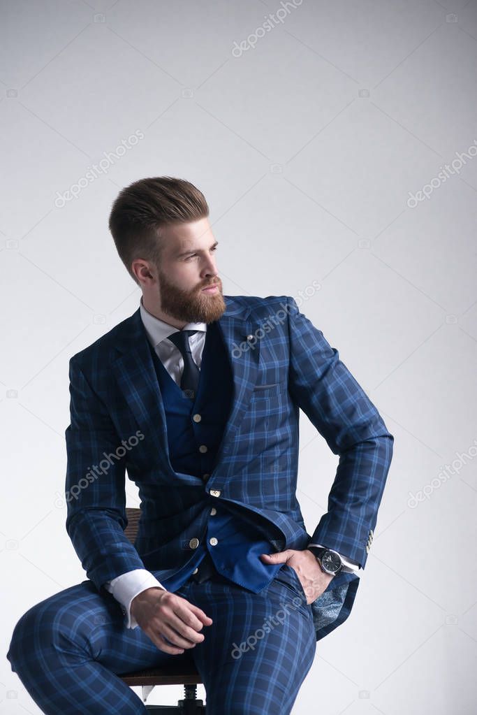He will melt your heart. Handsome young man in full suit and eyewear looking away while sitting on the stool