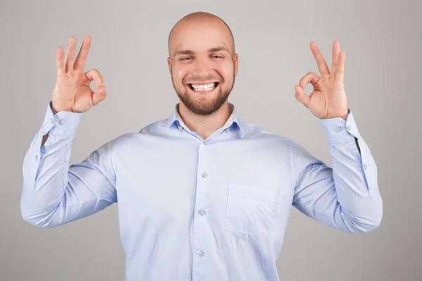 Retrato de un joven sonriente con camisa blanca mostrando un gesto aceptable mientras está de pie y mirando a la cámara aislada sobre un fondo blanco — Foto de Stock