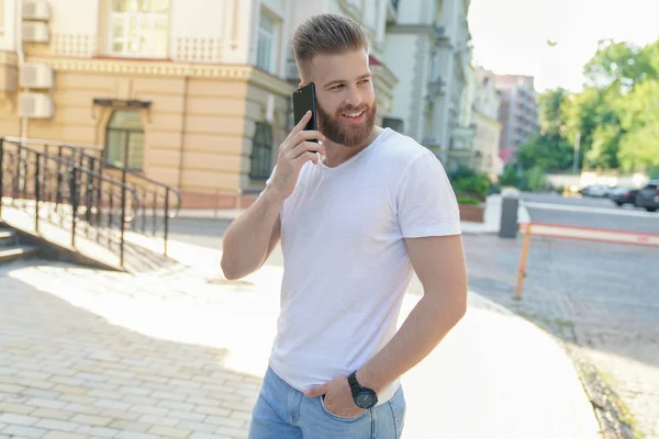 genç iyi görünümlü sakallı adam telefonda konuşurken ve gülümseyerek evinin önünde açık havada oturuyor.