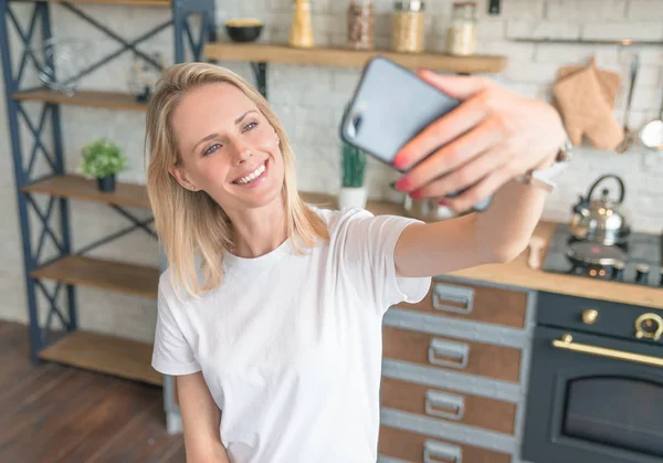 Belle jeune femme souriante faisant selfie avec le téléphone dans la cuisine. Une nourriture saine. cuisiner à la maison. Porter une chemise blanche . — Photo