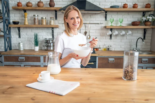 Sorrindo mulher saudável comer flocos de milho cereais enquanto sentado e tomando café da manhã na mesa da cozinha — Fotografia de Stock