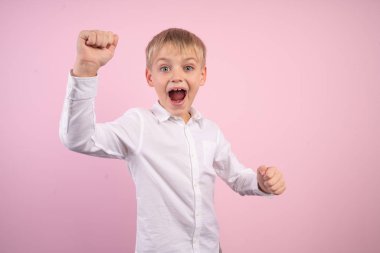 Funky güzel küçük çocuk portre yumruklar çığlık kaldırdı evet hedefleri olsun, piyango oyuncu yarışma yarışması, giyinmiş beyaz moda giyim izole pembe arka plan