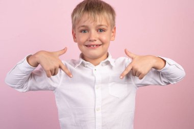 Mutlu küçük çocuk parmaklarını boş bir tişörte doğrulttu, reklam için bir yer. o pembe arka plan önünde duruyor