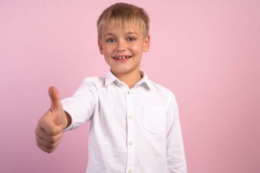 Mutlu küçük çocuk kameraya başparmak gösterir, reklam için bir yer. o pembe arka plan önünde duruyor