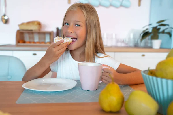 Милая маленькая девочка завтракает дома утром, ест пончик с чаем. вкусная еда . — стоковое фото