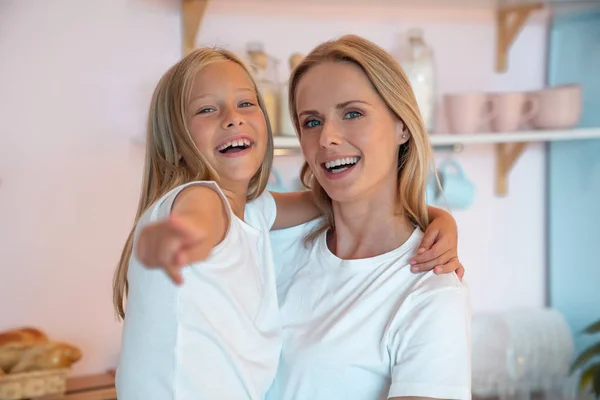 Mãe feliz e sua filhinha fofa estão se divertindo em casa sorrindo. Olha para ali. menina está apontando para algo interessante — Fotografia de Stock