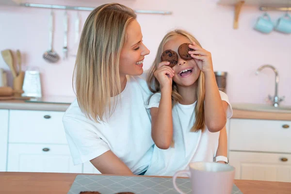 Ung mamma tittar på hennes lilla dotter ha kul att hålla Chocolate chip cookies och leende. Kärleksfull familj — Stockfoto