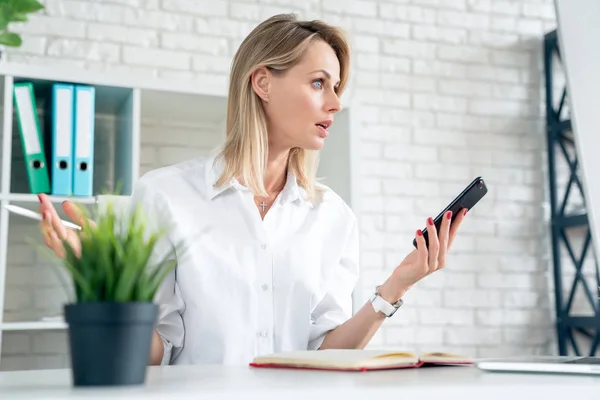 Young beautiful business woman disappointed looking at mobile phone while sitting at her working place