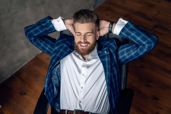 Tomando tiempo para un descanso minuto. Joven alegre sosteniendo las manos detrás de la cabeza y manteniendo los ojos cerrados mientras está sentado en su lugar de trabajo . — Foto de Stock