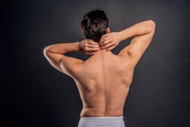 Yakışıklı, sakallı adam izole edilmiş. Üstsüz kaslı adam gri arka planda duruyor. Adamın boynunu tutuşu. Boyun ağrısı.