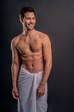 Yakışıklı, sakallı adam izole edilmiş. Üstsüz, havlulu kaslı adam gri arka planda duruyor. Ciddi adam başka tarafa bakıyor.