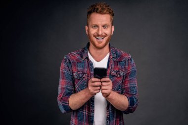 Adam bütün gün akıllı telefon oyununda oynuyor. Heyecanlı ve heyecanlı olmaya ara veremiyor. Gri duvardan mesaj yazarken cep telefonu ekranına bakan, günlük kıyafetli, yakışıklı, kızıl saçlı bir erkek..