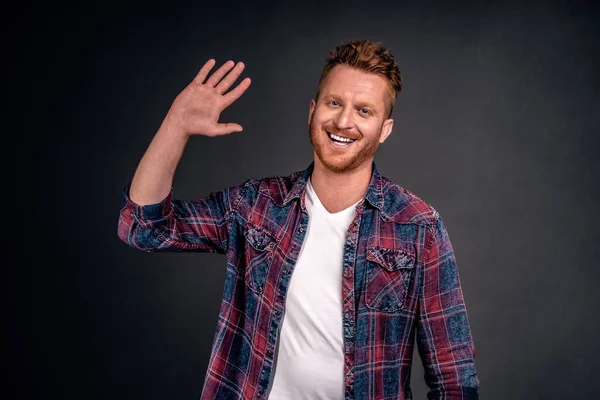 Handsome happy redhead man waiting for high five, smiling broadly raising palm high to greet person in modern way, welcoming close one over gray background, wearing trendy shirt.