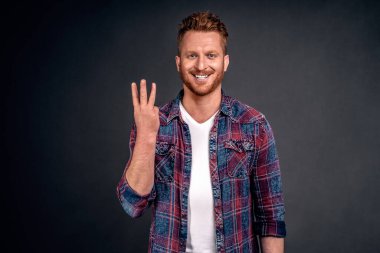 Beyaz tenli, sevimli, arkadaş canlısı, barmenden üç shot sipariş eden, üçüncüyü göstererek sırıtan, geniş bir gülümseme gösteren, arkadaşlarıyla birlikte barda dinlenen, gri arka planda oturan beyaz bir adam..