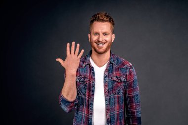 Henüz yüzük yok. Çekici, neşeli ve tasasız bekar portresi. Kısa saç stili. Beş el kaldırmış, geniş bir gülümseme sergiliyor..