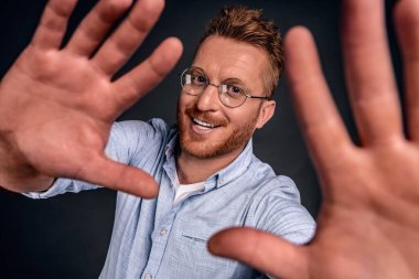 Adam selfie çekip internete yüklemeye çalışıyor. Tarz sahibi ve mutlu, sakallı ve şık saç kesimli yakışıklı bir adamın portresi. Kameraya doğru çekiliyor, sanki kendi fotoğrafını çekiyor, gülümsüyor gibi..