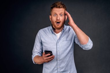 Adam aletin yapabileceklerinden etkileniyor. Eğlenceli ve mutlu, gözlüklü, beyaz gömlekli, sakallı, neşeli ve mutlu bir erkek başının ve akıllı telefonunun yanında el ele tutuşup, dudaklarını kıvırarak 