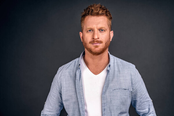 Headshot of handsome male freelancer with appealing look, has dark beard and mustache, looks directly at camera with serious look, wears white casual clothes. Facial expressions