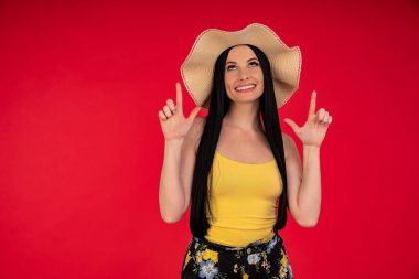 Yaz tatilindeki çekingen kız şaşırdı ve kırmızı arka planda izole edilmiş fotokopi alanını işaret etti.