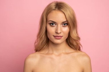 Güzel, üstsüz, uzun sarı saçlı, pembe arka planda soyutlanmış bir kadın. Güzellik konsepti.