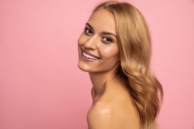 Güzel, üstsüz, uzun sarı saçlı, pembe arka planda soyutlanmış bir kadın. Güzellik konsepti.