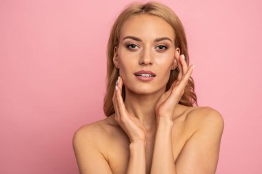 Güzel, üstsüz, uzun sarı saçlı, pembe arka planda soyutlanmış bir kadın. Güzellik konsepti.