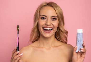 Diş fırçasıyla diş fırçası kullanan çekici bir kızın portresi pembe arka planda izole edilmiş kameraya bakıyor, günlük prosedür, bakım konsepti.