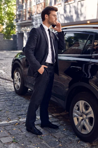 Confident business expert. Full length of handsome young businessman talking on the phone while standing near his car outdoors.