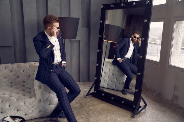 在家里的笼子里 坐在镜子旁边的沙发上 穿着蓝色西服的英俊男子 — 图库照片