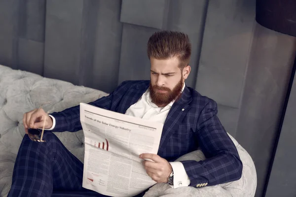 在家里的笼子里 穿着蓝色西装 坐在沙发上看新鲜报纸的英俊男子 — 图库照片