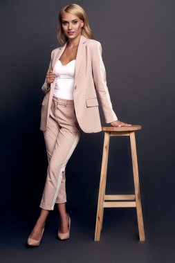 Kendinden emin ve modern. Gri arka planda poz verirken kameraya bakan tam boy genç kadın..