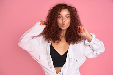 Şirin, kıvırcık saçlı, pembe arka planda komik surat yapan genç bir kız. Boşluğu kopyala