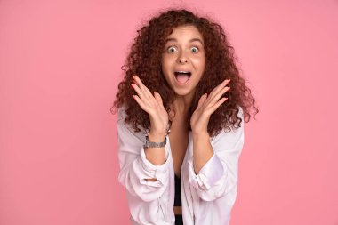 Kadınlar süper mutluluktan sakinleşemezler. Çekici, neşeli, kızıl saçlı kız arkadaş pozitif duygulardan parlıyor, yüzün yanında el ele tutuşuyor, şaşkınlıktan çenesini indiriyor, pembe duvarın üstünde heyecanlanıyor..