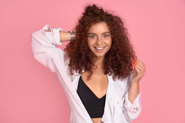 Mutlu, güzel bir kız. Gözleri kapalı gülümsüyor. Pembe arka planda kızıl kıvırcık saçlarına dokunuyor.