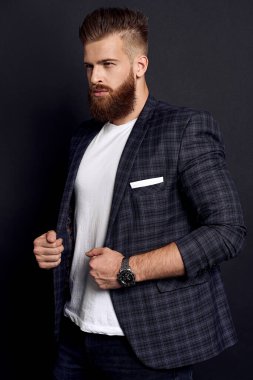 Mükemmel saçlı ve sakallı yakışıklı adam siyah arka planda dikilirken başka tarafa bakıyor..
