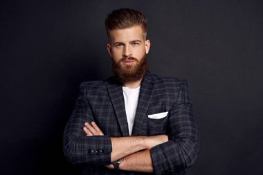 Yakışıklı adam kollarını kavuşturup gri arka planda dururken kameraya bakıyor..