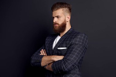 Gri arkaplana karşı profilde dururken kollarını çapraz tutan yakışıklı adam..