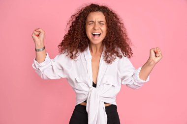 Hayret verici vahşi bir kadının yüksek sesle bağırması hiç adil değil, kollar öne doğru, seni öldürürüm, pembe arka planda izole edilmiş günlük kıyafetler giyerim.