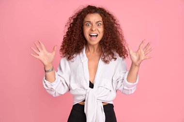 Hayret verici vahşi bir kadının yüksek sesle bağırması hiç adil değil, kollar öne doğru, seni öldürürüm, pembe arka planda izole edilmiş günlük kıyafetler giyerim.