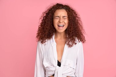 Hayret verici vahşi bir kadının yüksek sesle bağırması hiç adil değil, kollar öne doğru, seni öldürürüm, pembe arka planda izole edilmiş günlük kıyafetler giyerim.