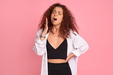 Yorgun, kızıl saçlı, yorgun, bitkin düşmüş, gözleri kapalı, uykulu görünen, kahve isteyen, pembe arka planda duran yorgun ve sıkılmış bir kız..