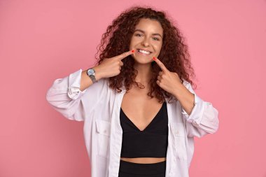 Benim güzel beyaz gülüşüme bak. Çekici genç bayan dişçiyi ziyaret etti diş tellerini çıkardı ve mutlu hissetti. Mükemmel bir sırıtışı var, pembe arka planda durup, ağzı işaret ediyor..