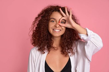 Kızıl saçlı kaygısız kadının yakın plan portresi gülümseyen, mutlu olumlu duygularını ifade eden, iyi bir jest eğilimi olan, sorun yaşamayan, rahat hisseden ve pembe arka planda keyif alan..