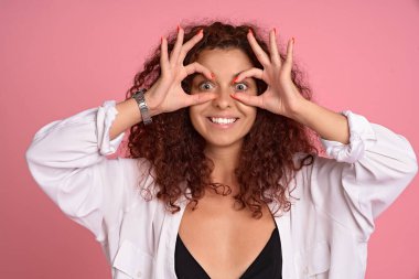 Kızıl saçlı kaygısız kadının yakın plan portresi gülümseyen, mutlu olumlu duygularını ifade eden, iyi bir jest eğilimi olan, sorun yaşamayan, rahat hisseden ve pembe arka planda keyif alan..