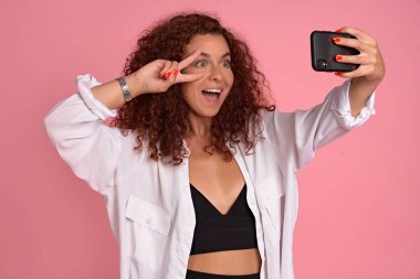 Kız takipçilerin önünde kendisi gibi davranmayı sever. Tasasız kızıl saçlı, şık kıyafetli, akıllı telefonuyla elini çeken, selfie çeken zafer işareti gösteren ve olumlu duygularını ifade eden birinin portresi..