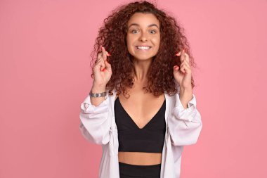 Hayalperest ve iyimser genç kız mucizelere inanır, şans diler ve dilek tutar, kameraya gülümseyen bir şekilde bakar, olumlu sonuçlar bekler, pembe arka planda durur..