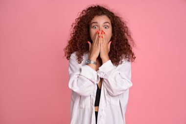 Güzel kızıl saçlı kız ağzını kapatıyor ve elleri pembe arka planda soyutlanıyor..